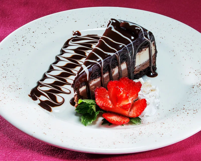 Desserts layered chocolate ganache cake garnished with strawberry rose and whipped cream