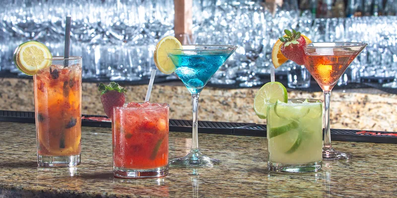 Five colorful cocktails in martini and rocks glasses on granite bar with citrus garnishes