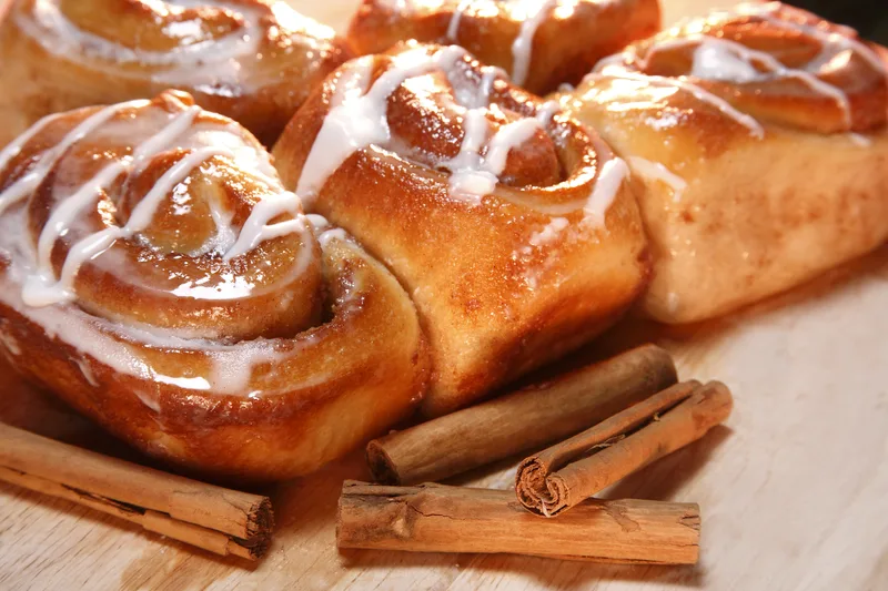 freshly baked cinnamon buns drizzled with white glaze beside cinnamon sticks