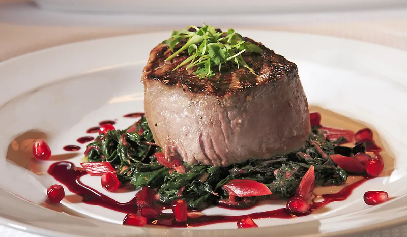 Seared filet mignon plated on wilted greens with pomegranate reduction