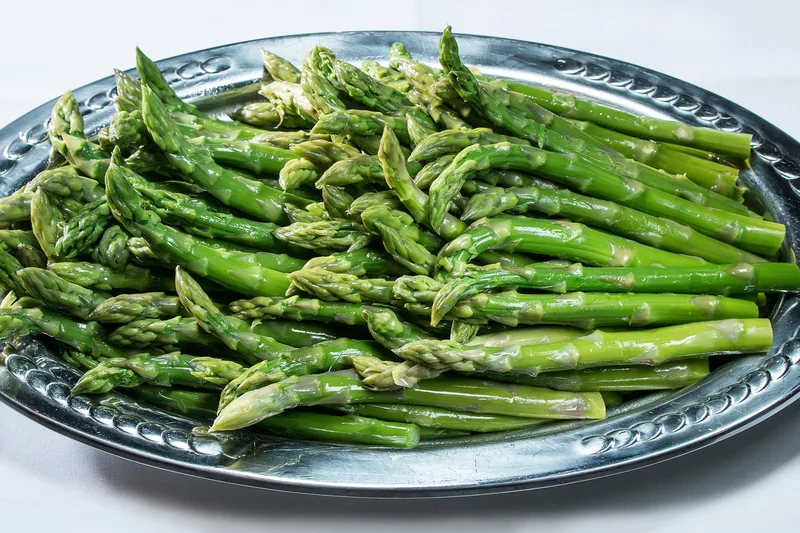steamed asparagus spears piled on ornate decorative stainless steel serving platter