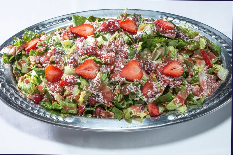 Brazilian salad with halved strawberries, shredded parmesan, and red vinaigrette on silver platter