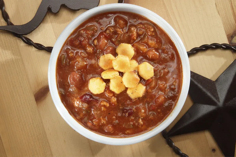 Texas chili with oyster crackers beside cast-iron star on wood surface