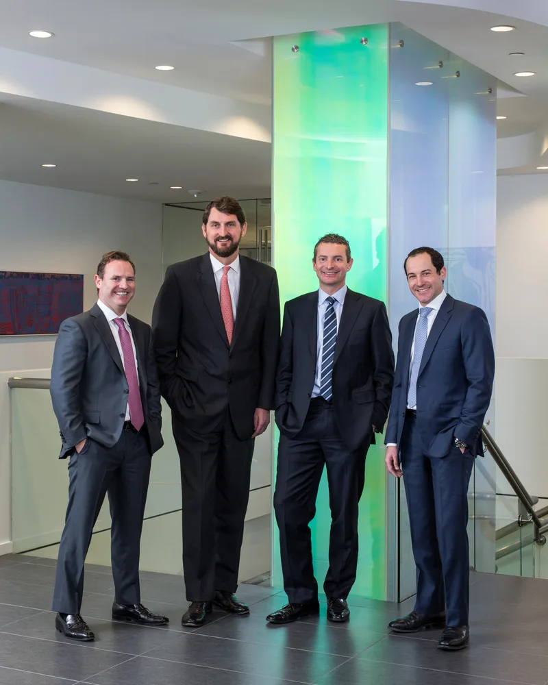 Four executives in tailored dark suits corporate group portrait modern office lobby