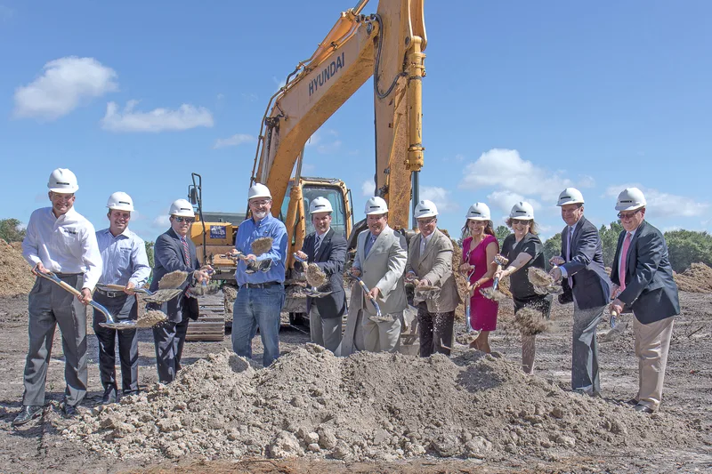 corporate groundbreaking ceremony professionals in hard hats lifting dirt with shovels