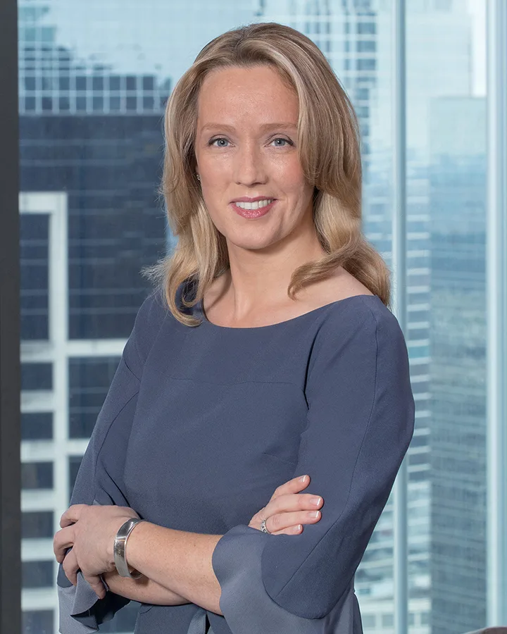On-site headshot woman gray top arms crossed office skyline background