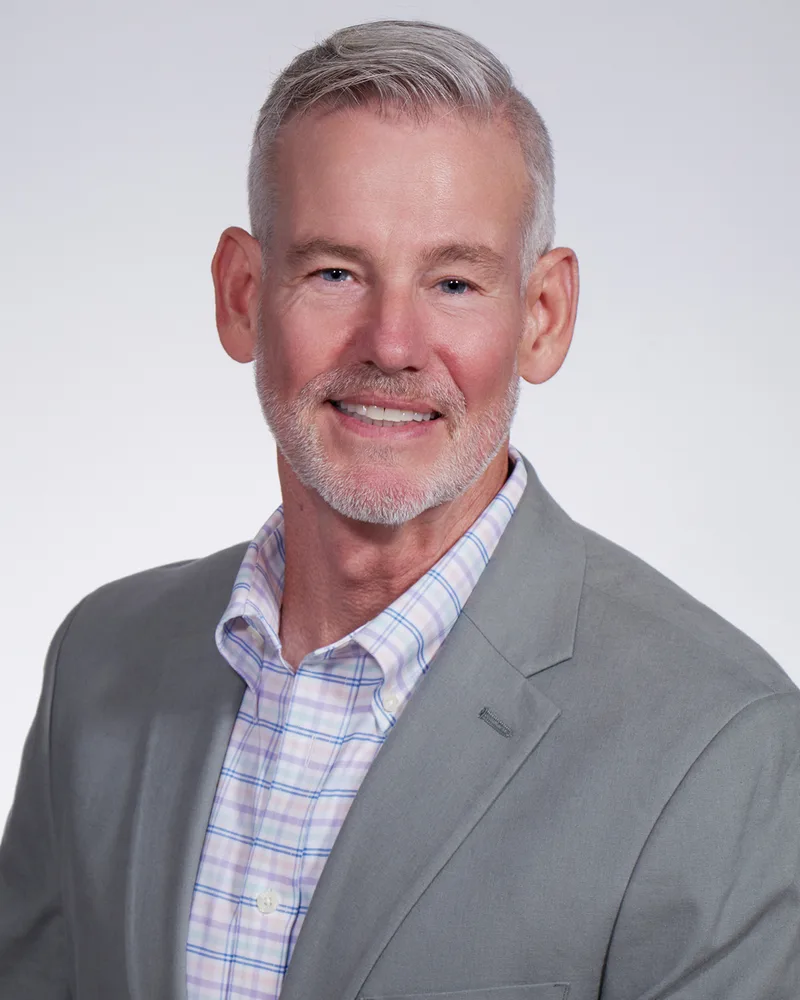 Casual business headshot silver-haired man gray blazer plaid shirt smiling