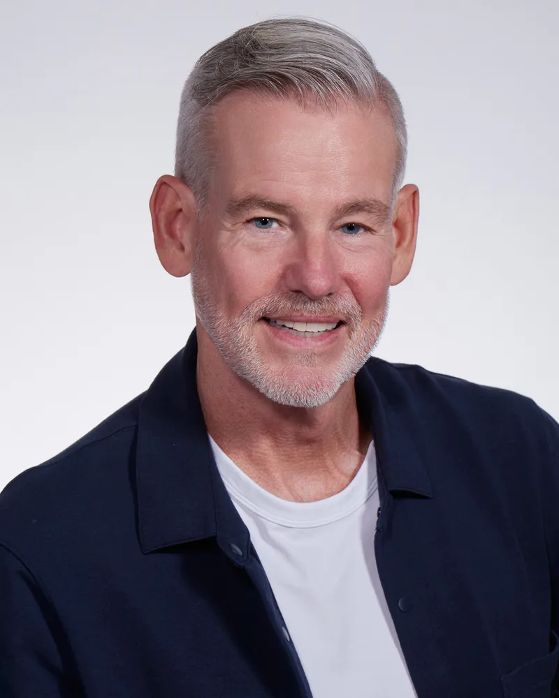 Casual headshot silver-haired man navy overshirt white tee light background