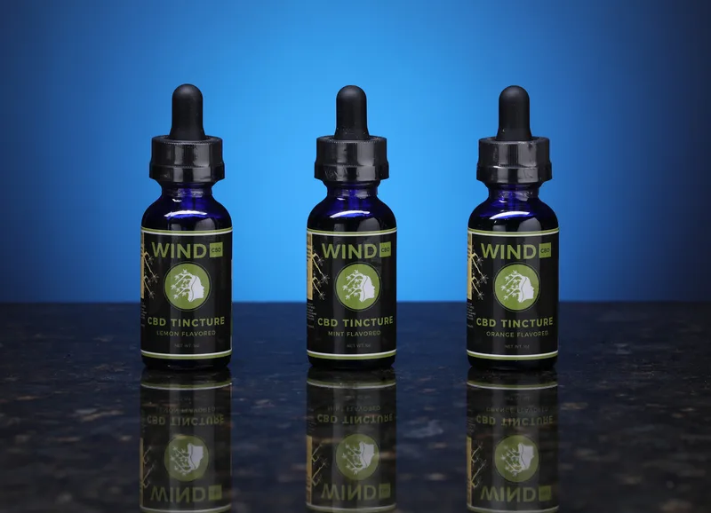 Wind CBD tinctures grouping three cobalt glass dropper bottles on reflective marble